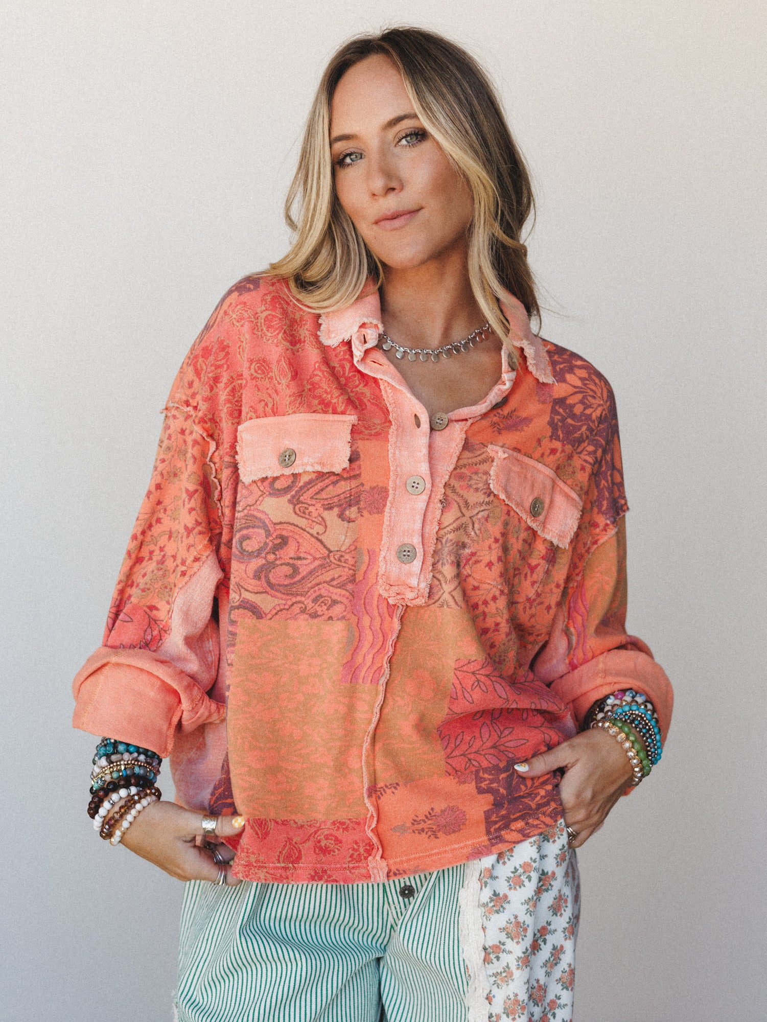 A patchwork oversized blouse in warm tangerine and plum tones worn with mixed-print pants and stacked boho bracelets — the kind of top that does all the talking.