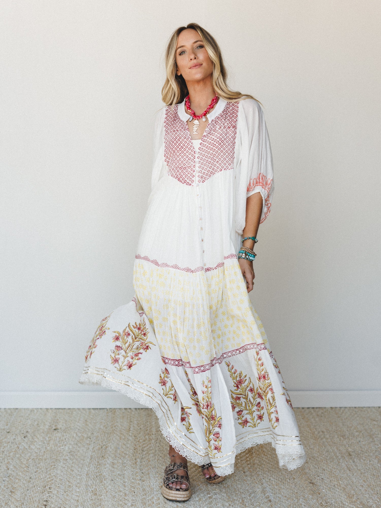 A flowy white maxi dress with block-print floral borders and a geometric embroidered bodice — the kind of dress that makes a Tuesday feel like a vacation somewhere warm.