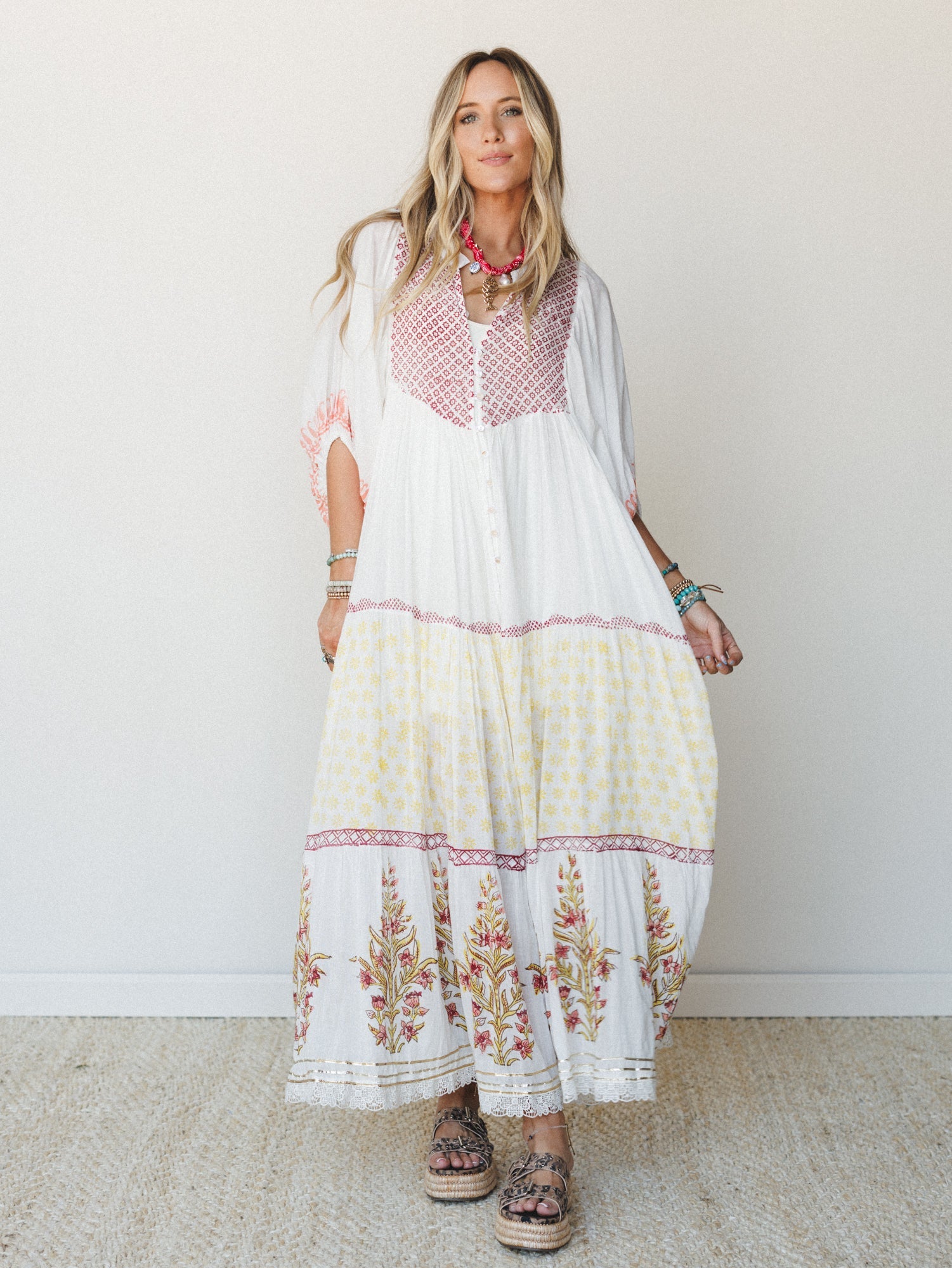 A breezy block-print maxi dress in white with pops of raspberry and yellow worn with platform espadrilles and layered turquoise and red jewelry — the kind of outfit that makes a farmers market feel like a vacation.