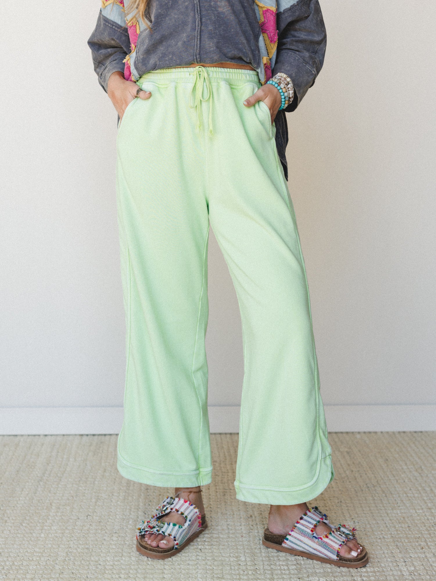 Wide-leg mint green sweat pants styled with beaded sandals and a graphic jacket — the kind of outfit that looks effortless but is clearly very much on purpose.