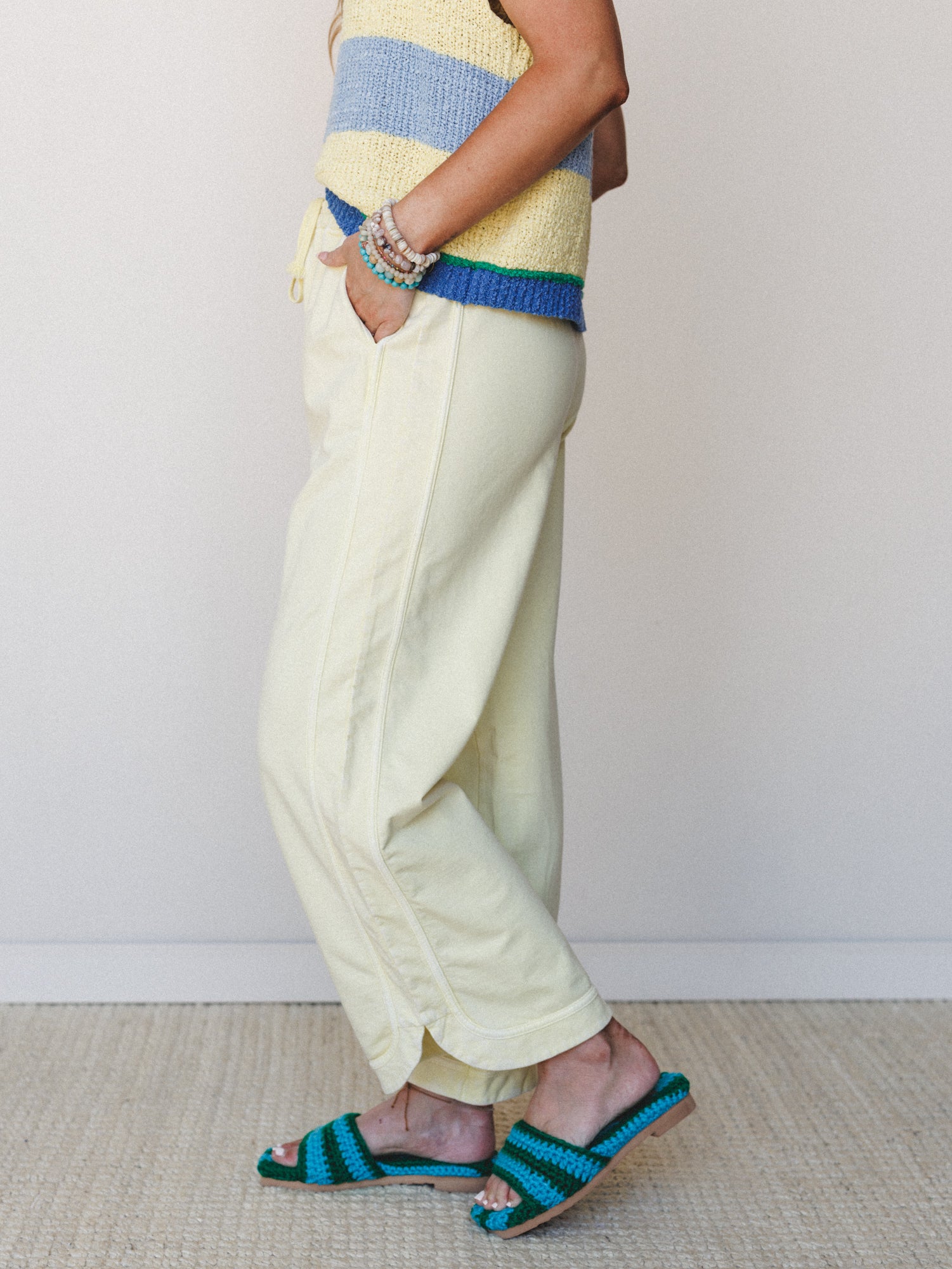 A side-profile shot of a model in butter yellow wide-leg pants paired with a color-blocked striped knit top and crochet slide sandals — the whole look has that easy, sunny energy of a good Saturday with nowhere to be.