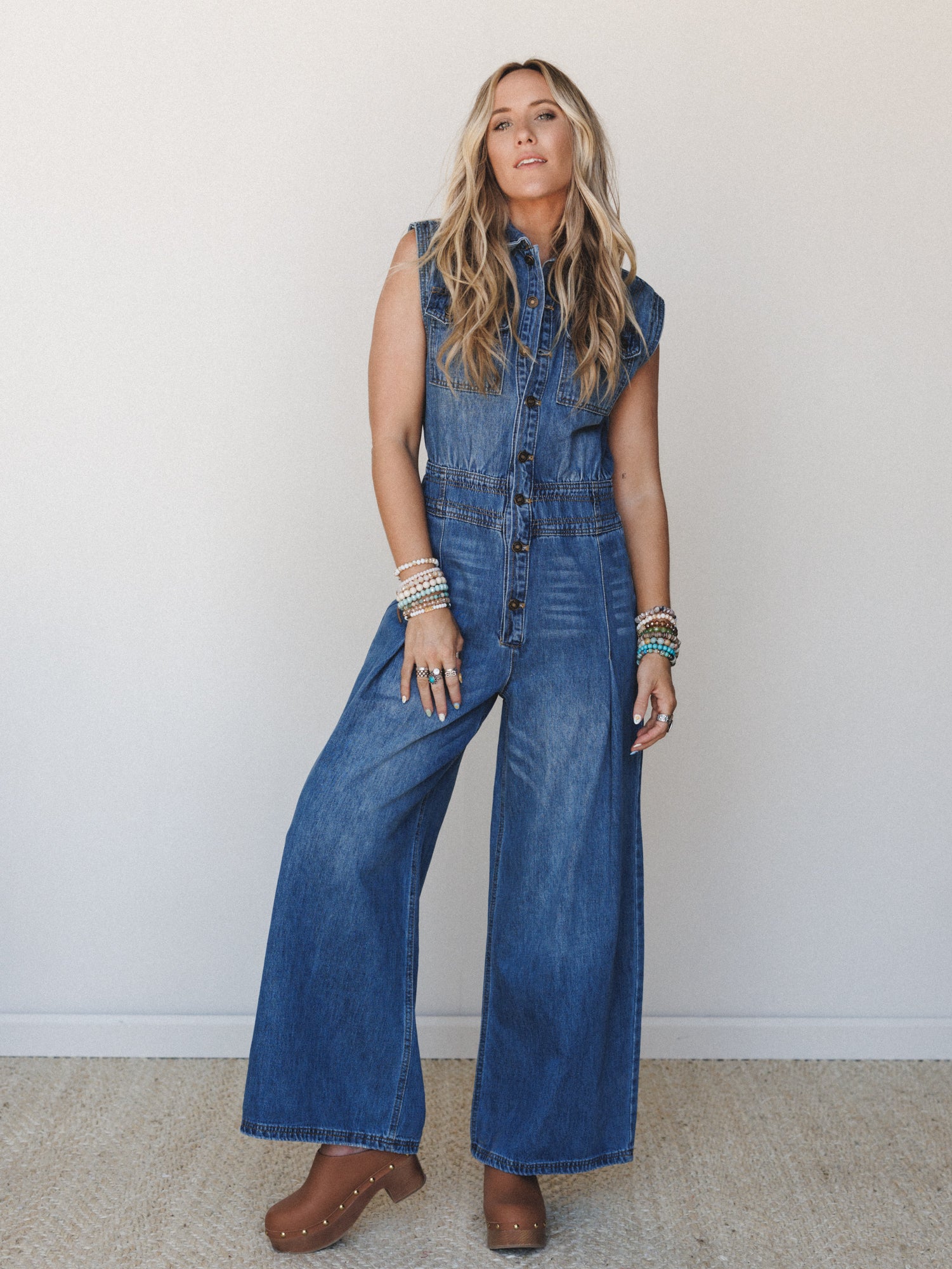 A wide-leg denim jumpsuit styled with stacked boho bracelets and studded clogs — the kind of outfit that feels effortless but clearly had some thought behind it.