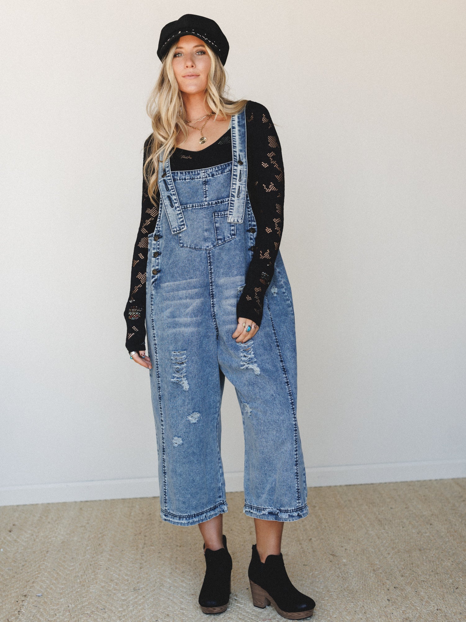Acid-washed denim overalls styled with a black crochet long-sleeve top, baker boy hat, and black ankle booties — the kind of outfit that feels effortless but clearly had a thought behind it.