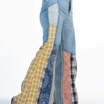 A person wearing Magnolia Patchwork Jeans - Washed Denim featuring mixed patterns and colors with a frayed hem, styled with sandals and layered bracelets.