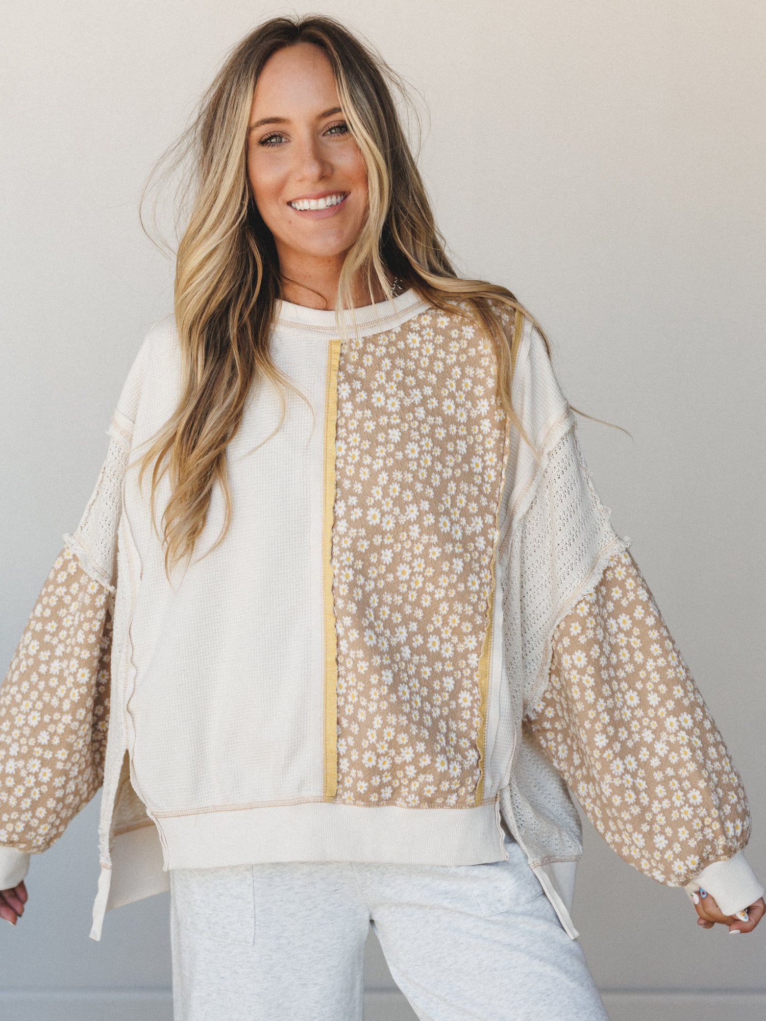 A mixed-media pullover top in cream and tan with daisy floral panels, worn with light grey joggers — the kind of top that makes a Sunday errand run feel like a whole moment.