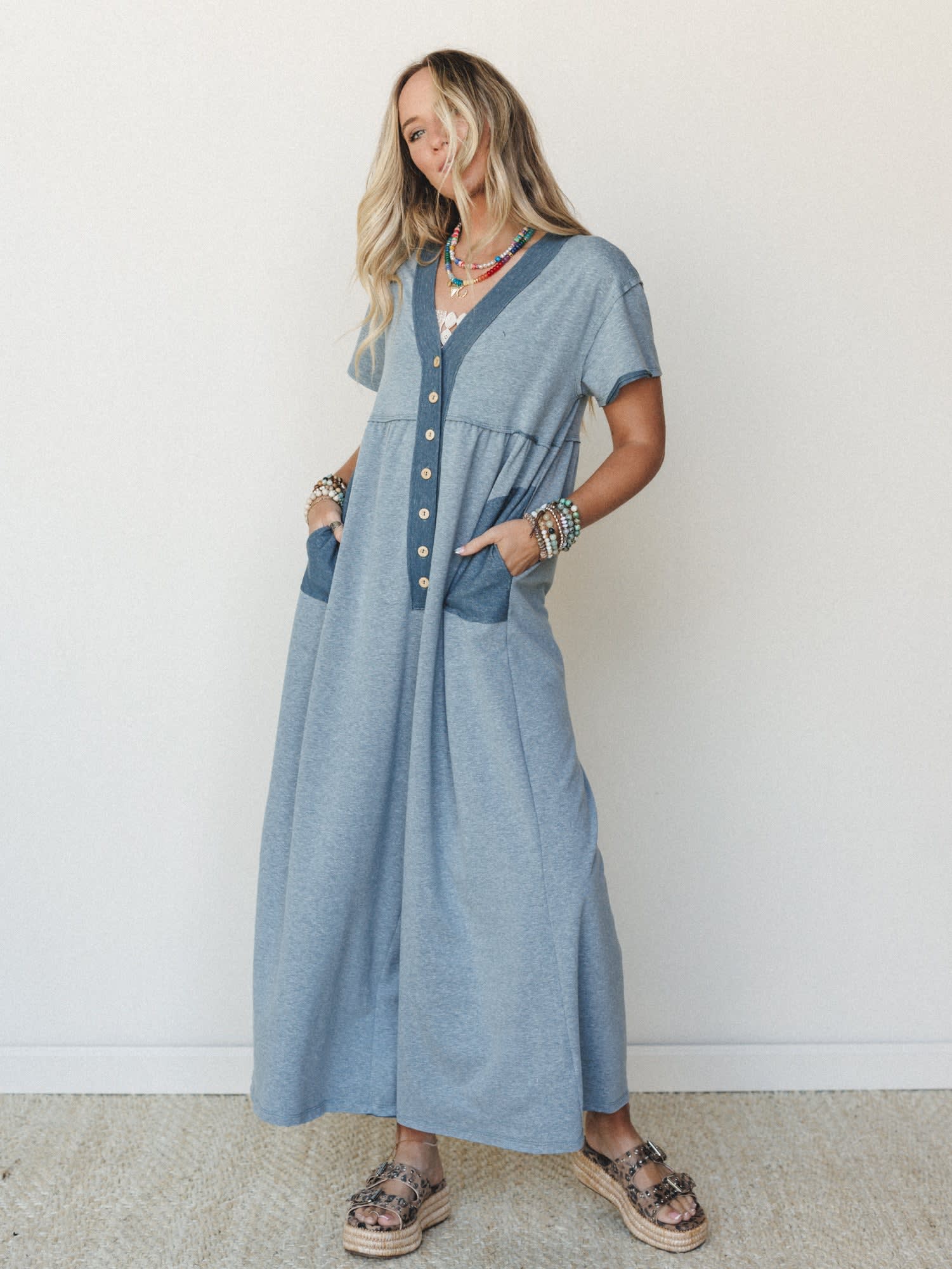 A relaxed maxi-length button-front dress in heathered dusty blue styled with layered beaded necklaces, stacked bracelets, and espadrille platform sandals — the kind of outfit that looks effortless but clearly wasn't an accident.