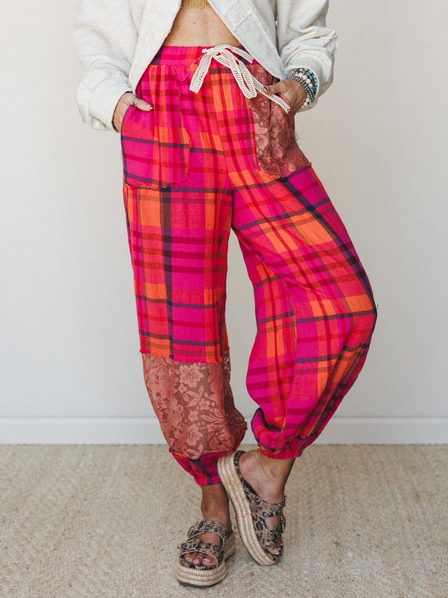 Bold pink plaid harem-style pants with lace patchwork panels steal the show, styled with a cream cropped sweatshirt and leopard print espadrille sandals for a playful, expressive everyday look.