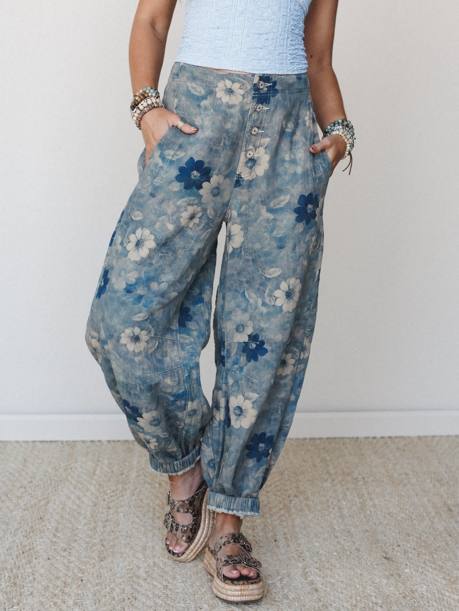Relaxed floral denim pants in a washed indigo print styled with a pale blue textured crop top, stacked bracelets, and studded espadrille sandals — the kind of outfit that looks effortless but clearly wasn't an accident.