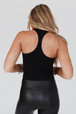 A woman with long blonde hair is seen from the back, wearing the High Neck Racerback Brami in black and high-waisted faux leather pants, accessorized with multiple bracelets, against a plain white background.