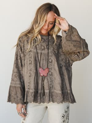 A flowy eyelet blouse in washed mushroom brown styled with embroidered cream jeans and a butterfly pendant necklace — the kind of top that looks like it's been loved for years and somehow still gets better.