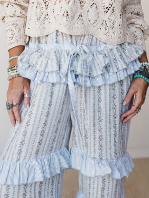 A close-up of flowy wide-leg pants in a soft blue floral stripe, styled with a crochet top and stacked turquoise and silver jewelry — the kind of outfit that feels romantic without trying too hard.