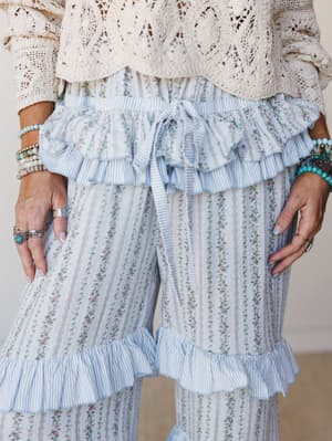 A close-up of flowy wide-leg pants in a soft blue floral stripe, styled with a crochet top and stacked turquoise and silver jewelry — the kind of outfit that feels romantic without trying too hard.