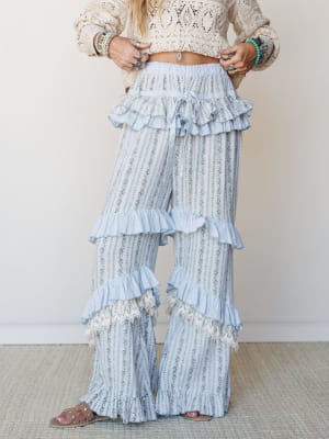 Wide-leg ruffle pants in a soft blue floral stripe print styled with a cream crochet crop top and turquoise jewelry — the kind of outfit that feels like a summer afternoon with nowhere to be.