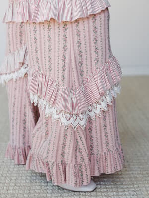 A close-up detail shot of wide-leg floral stripe pants with layered ruffle tiers, red-and-white ticking stripe ruffles, and scalloped eyelet lace trim — romantic and cottagecore-leaning with a seriously pretty mix of prints.