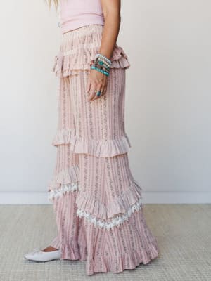 A side-profile shot of a tiered, floral-stripe maxi skirt styled with a blush pink ribbed tank and stacked turquoise bracelets — soft, romantic, and the kind of outfit that makes a Saturday feel like an event.