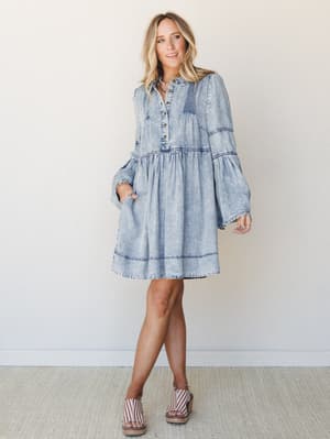 A light acid-wash denim mini dress with boho-western energy — tiered silhouette, bell sleeves, and pintuck detailing styled with striped platform wedges for an effortlessly put-together warm-weather look.