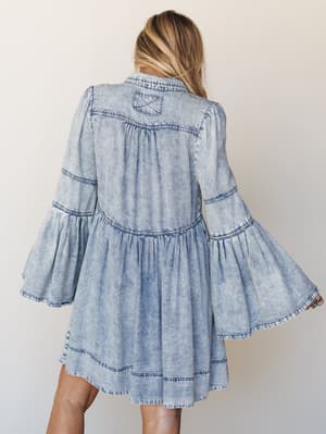 A back-view shot of a tiered acid-wash denim mini dress with dramatic bell sleeves — equal parts western and free-spirited, the kind of piece that looks just as good at a concert as it does on a dusty afternoon drive.