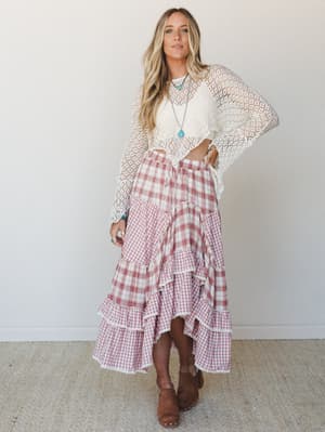A breezy, lived-in look built around a mixed plaid and gingham tiered maxi skirt in dusty rose and cream, styled with an open-knit crochet top, turquoise pendant necklace, and wood-sole clogs — the kind of outfit that looks like it came together effo
