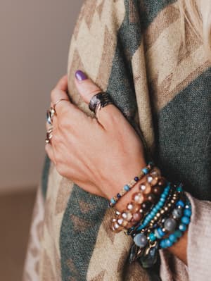 Close-up of a hand wearing multiple bracelets and a ring, holding a patterned scarf.