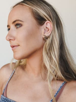 A close-up profile shot highlighting a gold bird stud earring against a soft neutral backdrop — the kind of piece that quietly becomes someone's everyday signature.