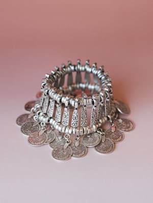 A chunky silver coin bracelet photographed solo against a dusty rose gradient background — the kind of piece that looks like it was found at a market in another country and never taken off.