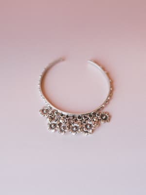 A silver cuff bracelet with dangling flower charms photographed against a soft blush background — the kind of piece that makes an outfit feel intentional without trying too hard.