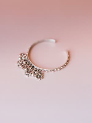 A silver cuff bracelet with dangling floral charms and a beaded band rests against a soft blush background — the kind of piece that looks like it was found at a market and worn every day since.