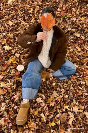 Person sitting on a bed of autumn leaves holding a leaf over their face.