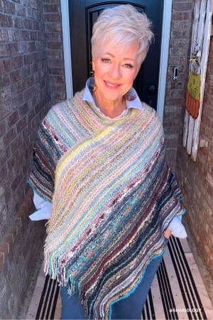 Woman wearing a colorful knitted shawl standing in front of a door.