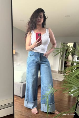 Woman taking a mirror selfie wearing a white top and blue jeans indoors.