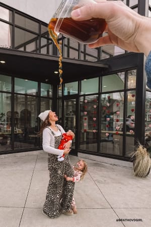 Person pouring a dark liquid from a small container into a glass, with a woman and child in the background.