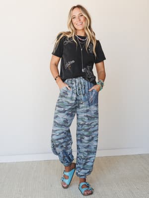 A relaxed, western-inspired outfit pairing a washed black graphic tee with roomy camo jogger pants, turquoise Birkenstocks, and layered beaded jewelry — the kind of look that feels effortless and a little unexpected.