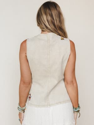 Back view of a washed sand denim vest with small embroidered patches, styled with a white textured skirt and stacked turquoise bead bracelets — easy, expressive, and a little western-inspired.