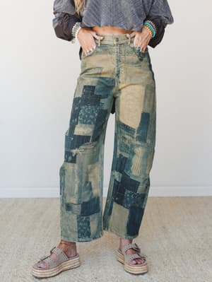 Patchwork barrel-leg jeans in a worn vintage wash styled with a cropped gray top, platform espadrille sandals, and layers of turquoise and beaded bracelets — the kind of pants that look like they've been somewhere interesting.