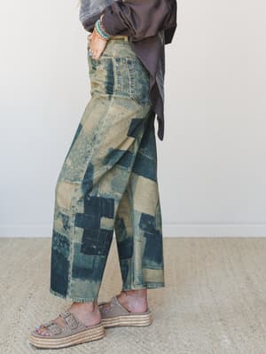 A side-profile shot of wide-leg barrel jeans in a heavily washed patchwork denim, styled with a slouchy mauve sweatshirt, stacked turquoise bracelets, and platform espadrille sandals — the kind of outfit that looks effortless but was absolutely thoug