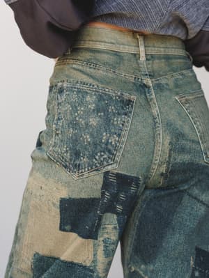 A close-up back view of heavily washed wide-leg jeans with patchwork-style print detailing and a lived-in, sun-bleached finish — the kind of jeans that look like they've been somewhere interesting.