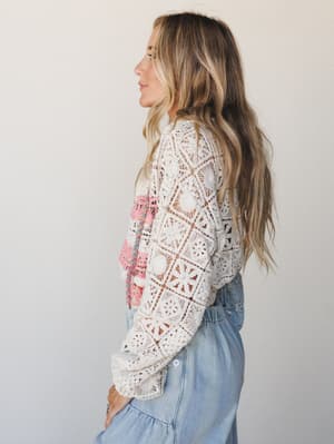 A side-profile shot of a model in a cream crochet open-front jacket layered over a colorful graphic tee, paired with light wash denim — relaxed, boho, and the kind of outfit that makes a regular Tuesday feel intentional.