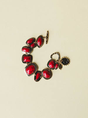 A bold statement bracelet laid flat, featuring chunky red crackle stone cabochons set in silver-tone links with a toggle clasp and small peace sign charm — the kind of piece that turns a plain outfit into a whole personality.
