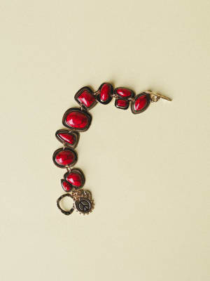 A chunky stone-link bracelet with deep red crackled cabochon stones set in dark gunmetal frames, finished with a dangling peace sign charm — the kind of piece that makes a plain white tee feel intentional.