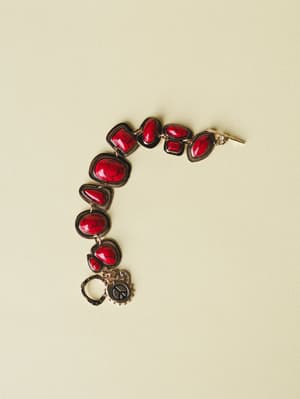 A chunky stone-link bracelet with deep red crackled cabochon stones set in dark gunmetal frames, finished with a dangling peace sign charm — the kind of piece that makes a plain white tee feel intentional.