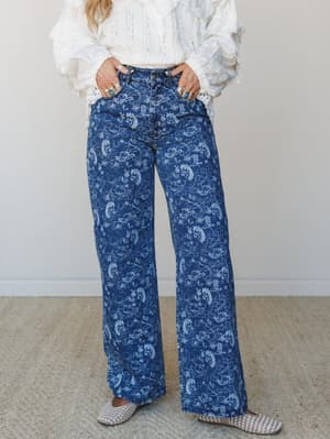 Wide-leg printed denim styled with a ruffled white lace top and woven mules — the kind of outfit that looks effortless but has clearly been thought about, stacked rings and all.