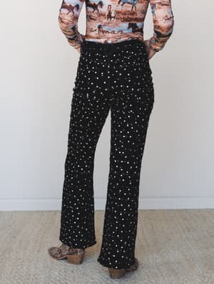 Shot from behind, a model pairs all-over sequin-embellished black flare jeans with a horse-print long-sleeve top and leopard ankle boots — the kind of outfit that quietly does the most.