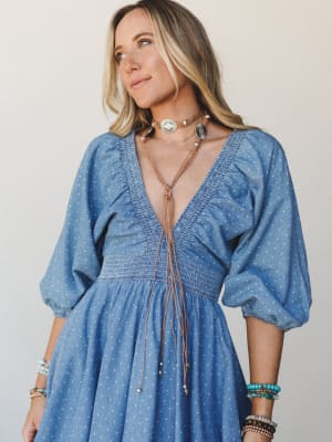A breezy blue polka dot dress with a deep v-neck and smocked waist, styled with stacked turquoise and beaded bracelets and a layered boho choker necklace — the kind of outfit that feels effortless and intentional at the same time.