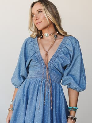 A breezy blue polka dot dress with a deep v-neck and smocked waist, styled with stacked turquoise and beaded bracelets and a layered boho choker necklace — the kind of outfit that feels effortless and intentional at the same time.