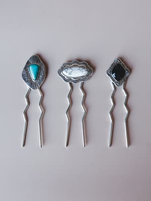 Three silver hair pins laid flat against a soft grey background, each topped with a different stone setting — turquoise, white howlite, and black onyx — with intricate stamped metalwork that feels equal parts western and heirloom.
