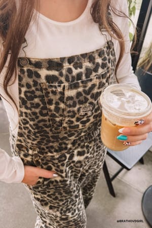 Person wearing leopard print overalls holding a coffee cup.