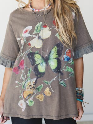 A washed ash brown graphic tee with a vintage botanical butterfly print, styled with layered beaded necklaces and stacked bracelets — the kind of top that looks like it's been loved for years and somehow keeps getting better.