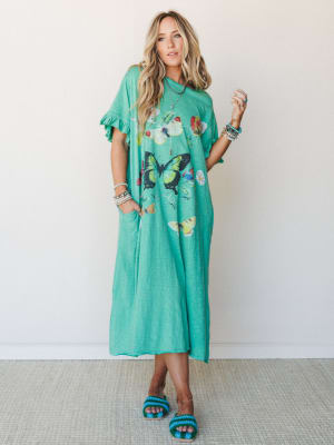 A relaxed, oversized maxi dress in bright kelly green with a scattered butterfly graphic print, styled with stacked bracelets and crochet slide sandals — effortless and a little whimsical, like a summer afternoon with nowhere to be.