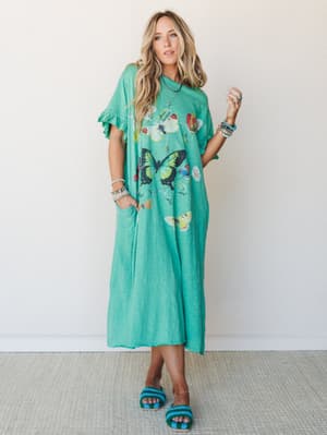 A relaxed, oversized maxi dress in bright kelly green with a scattered butterfly graphic print, styled with stacked bracelets and crochet slide sandals — effortless and a little whimsical, like a summer afternoon with nowhere to be.