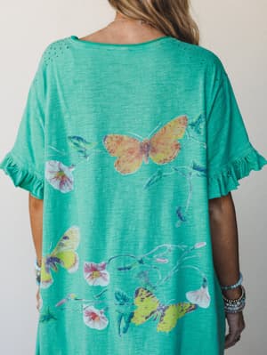 A close-up of the back of a bright mint green maxi dress covered in a watercolor butterfly and floral vine print, with sweet ruffle sleeve hems and delicate eyelet detail at the shoulders — the kind of dress that makes you want to go somewhere with g